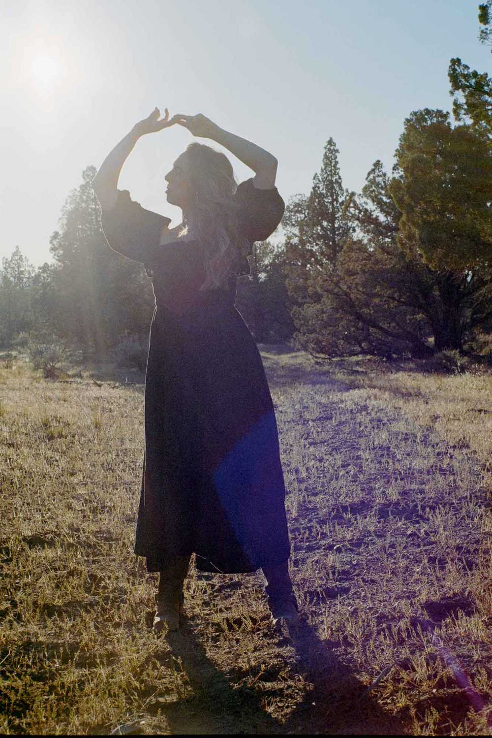 Backlit film photography portrait of a woman in a black dress surrounded by Juniper trees