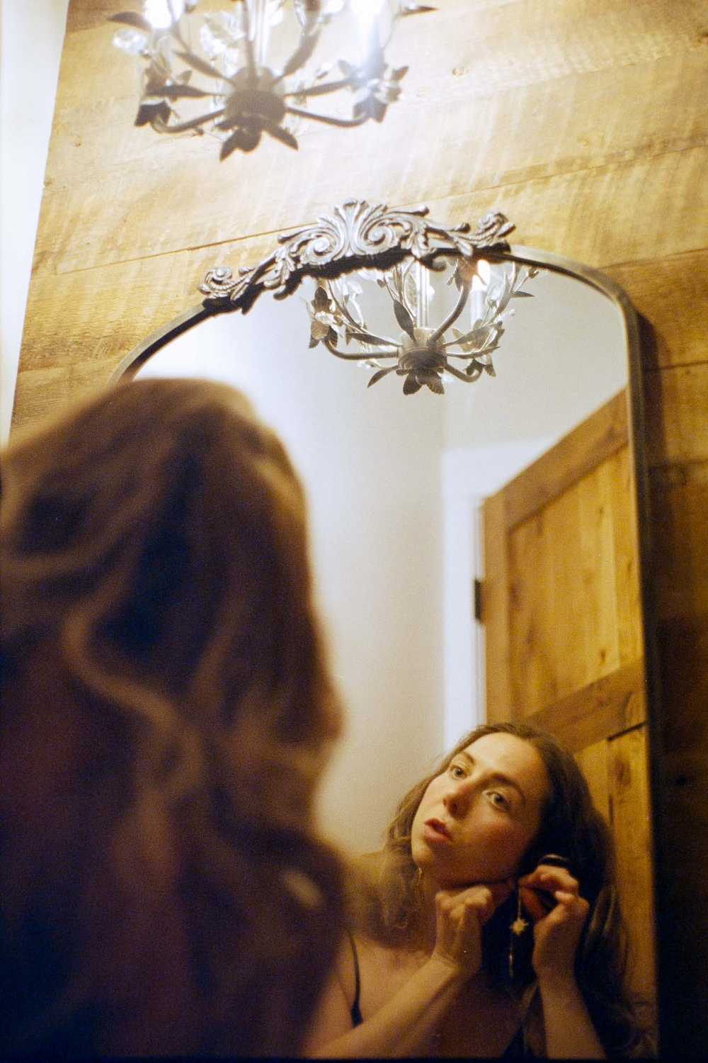 Romantic film photography portrait of a woman getting ready in front of a mirror