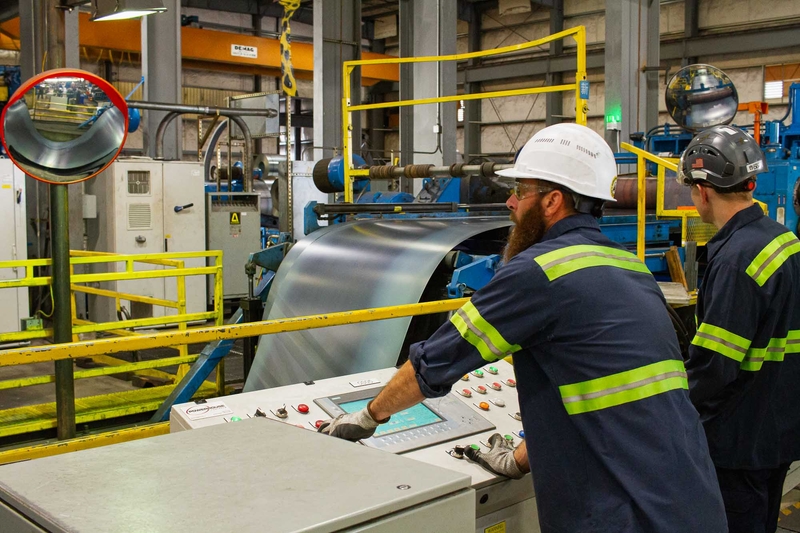 Workers monitoring a machine at Oregon Metal Services in Portland, OR